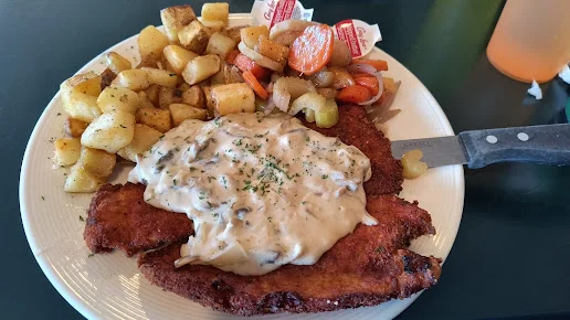 Schnitzel topped with a creamy mushroom sauce, with home fries and vegetables