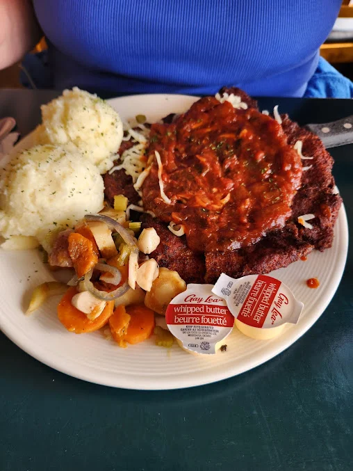Schnitzel topped with tomato sauce and cheese, with mashed potatoes and vegetables